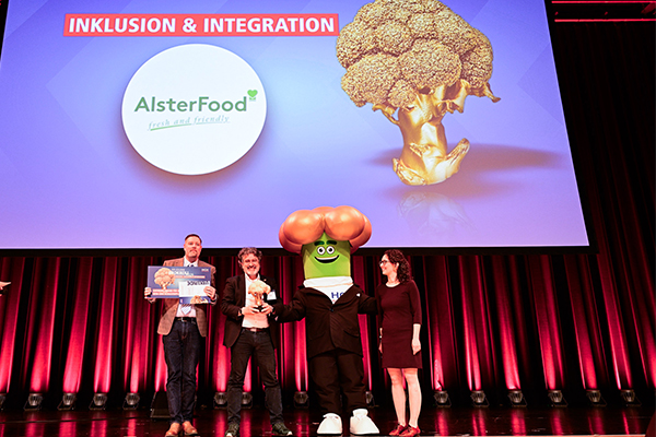Die Vertreter von GenussInklusiv und AlsterFood (Amedeus Hajek, m.), Gewinner Goldener Brokkoli 2026 in der Kategorie Inklusion und Integration, mit Laudatorin Simone Scharfenberg.